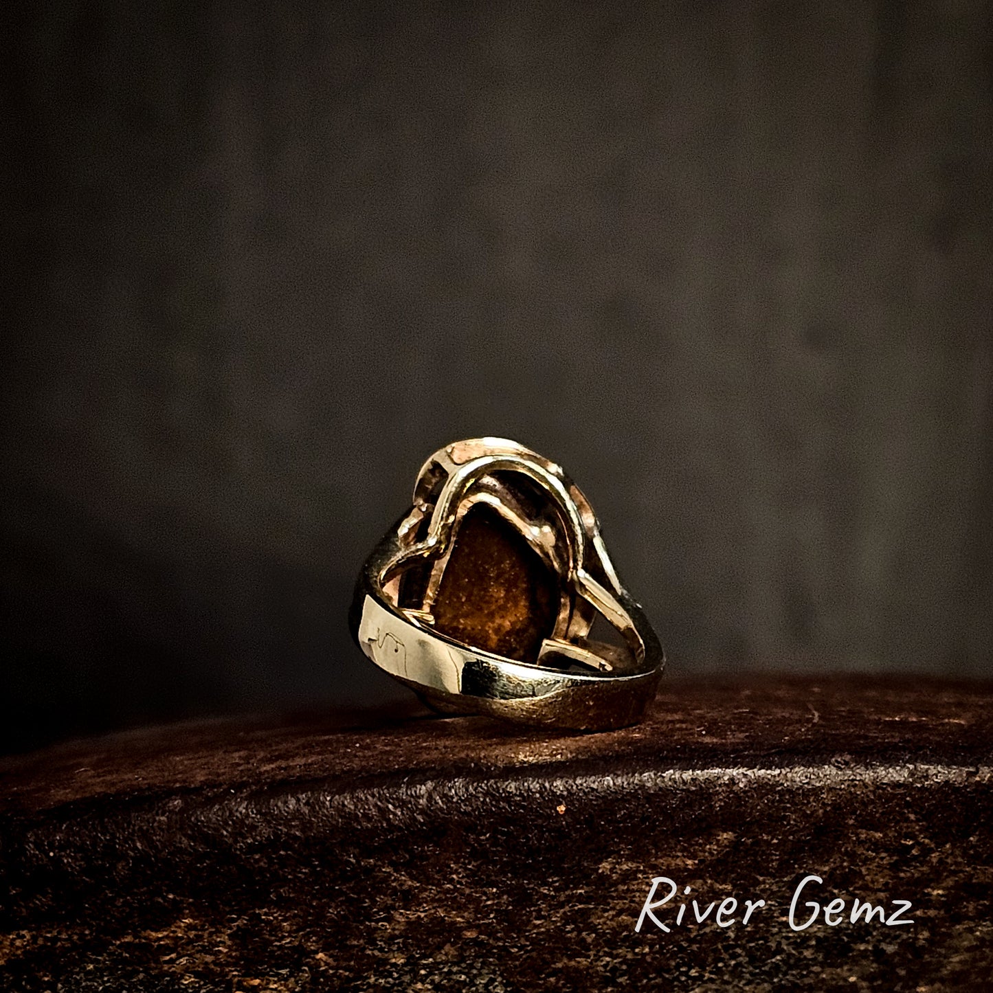 Back of gold ring showing the ironstone matrix of the included boulder opal on an cast iron surface, branded 'River Gemz'.
