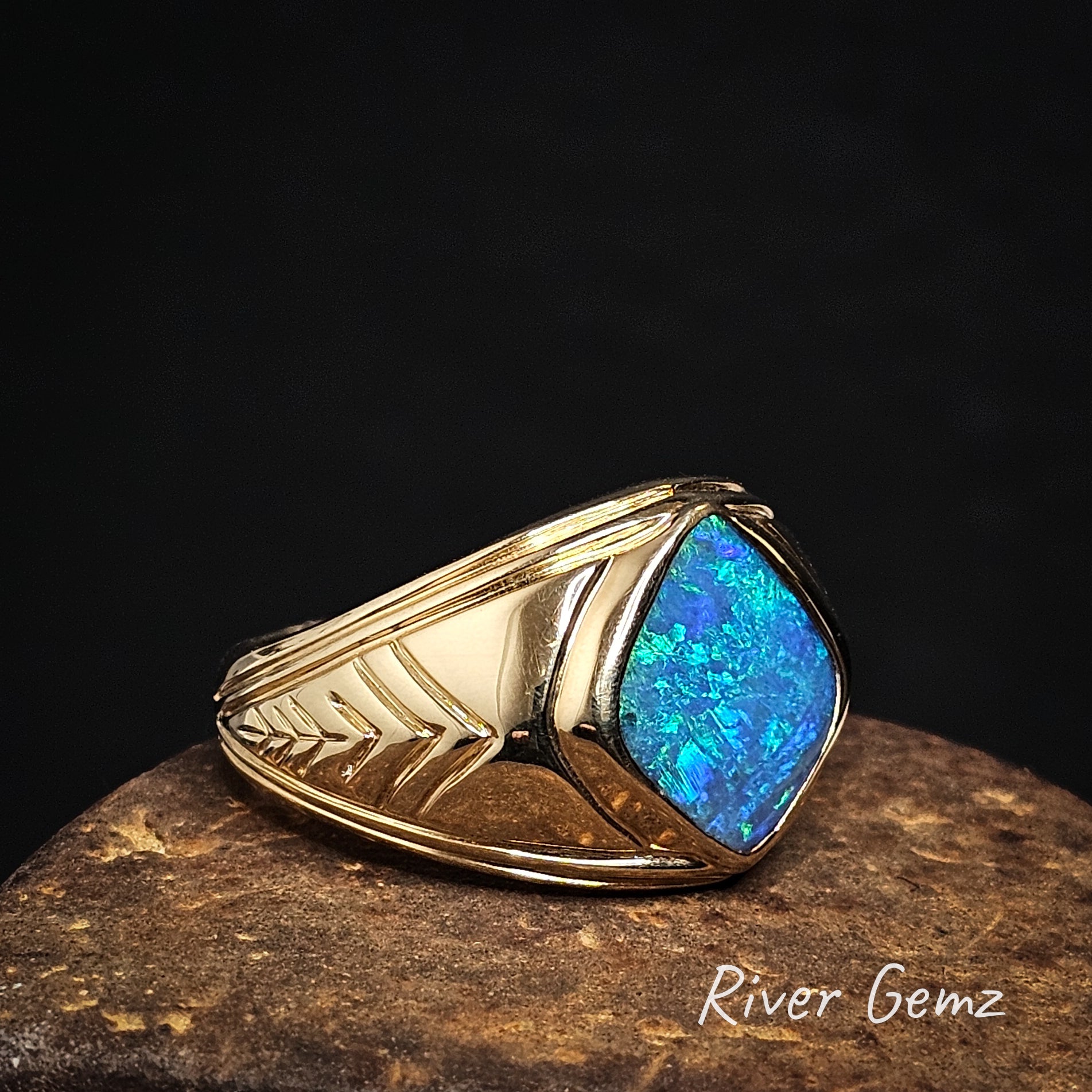 Large gold ring with a blue opal stone on a dark background.
