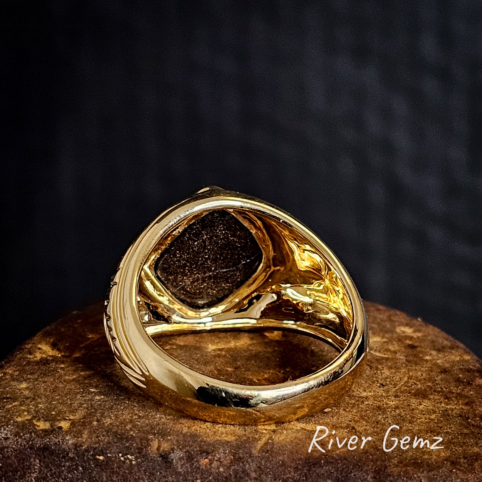 Rear of gold ring showing the ironstone matrix of the embedded boulder opal on a rusty surface, branded 'River Gemz'.