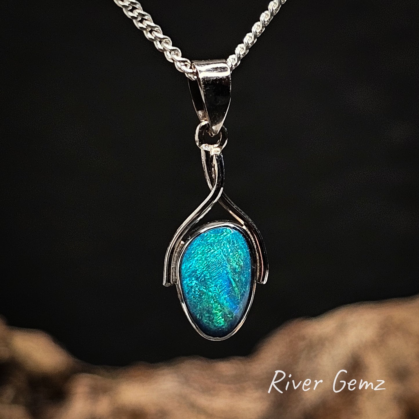 White gold pendant with a blue and green opal on a dark background, featuring 'River Gemz' branding.