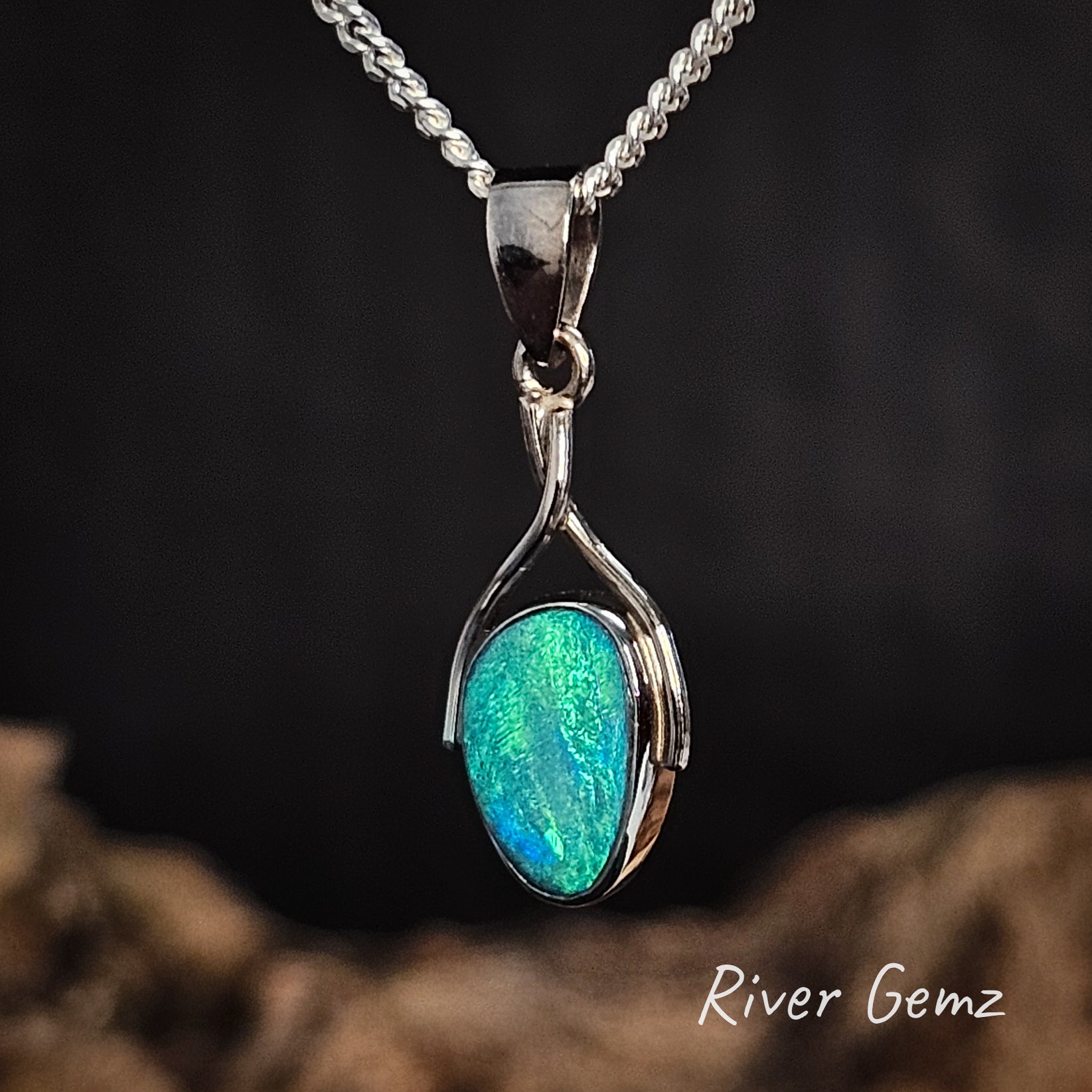 Green boulder opal set in white gold pendant on a dark background, featuring the brand 'River Gemz'.