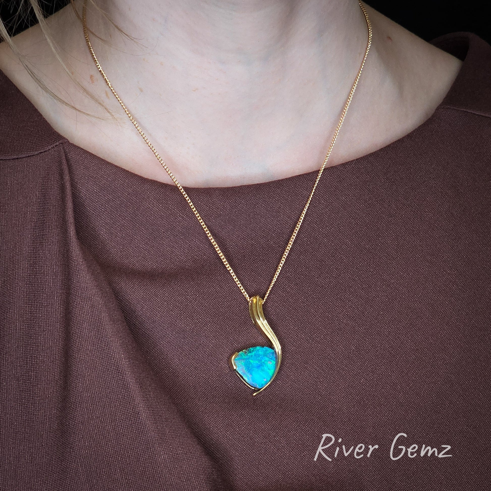 Triangular blue and green opal set in high grade yellow gold pendant worn by a person.
