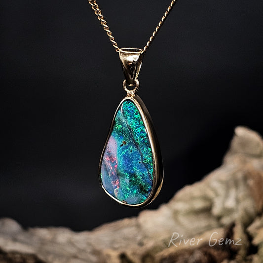 Teardrop-shaped opal pendant on a gold chain against a dark background with 'River Gemz' branding.