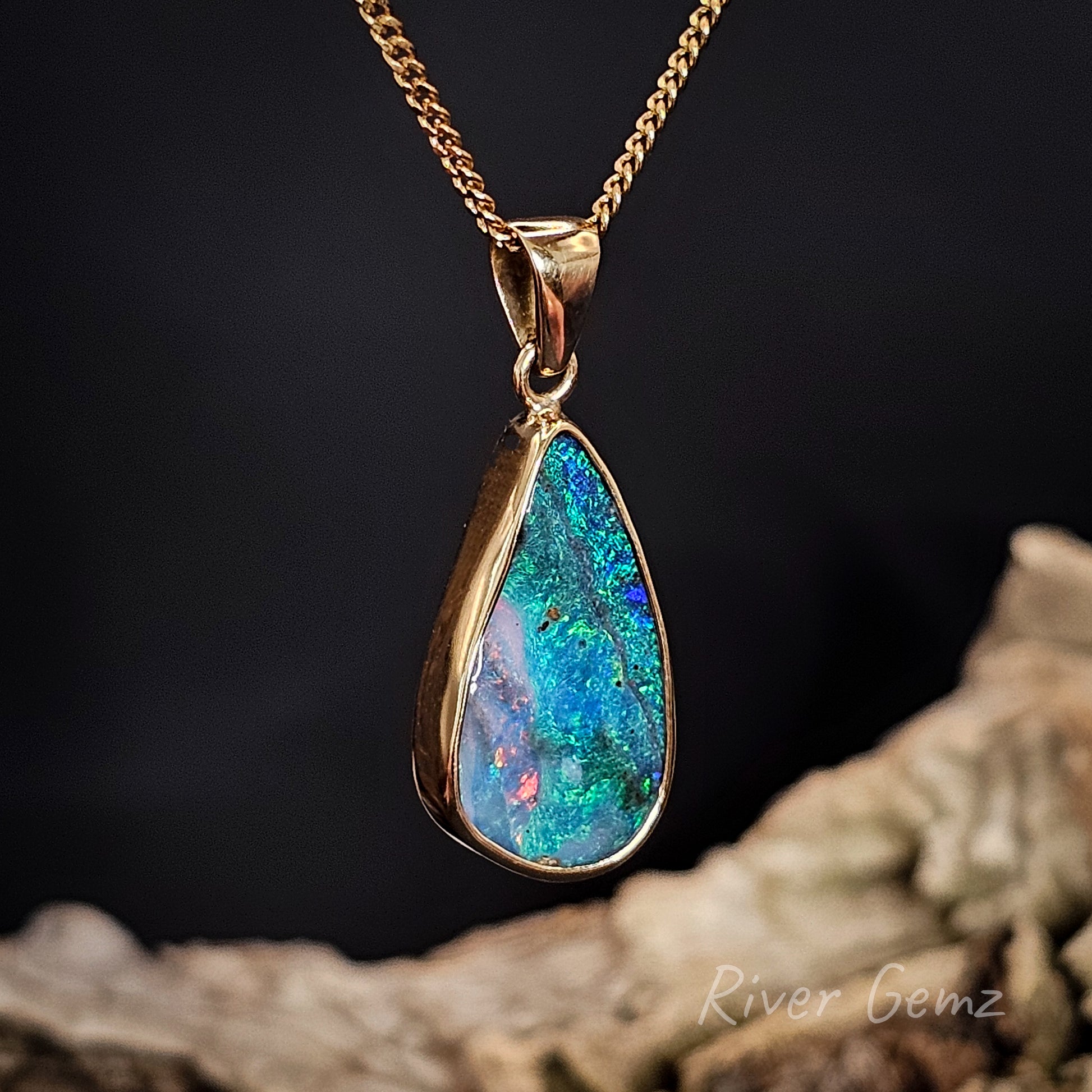 Colourful opal full besel set in yellow gold necklace with a large bail on a dark background with 'River Gemz' branding.