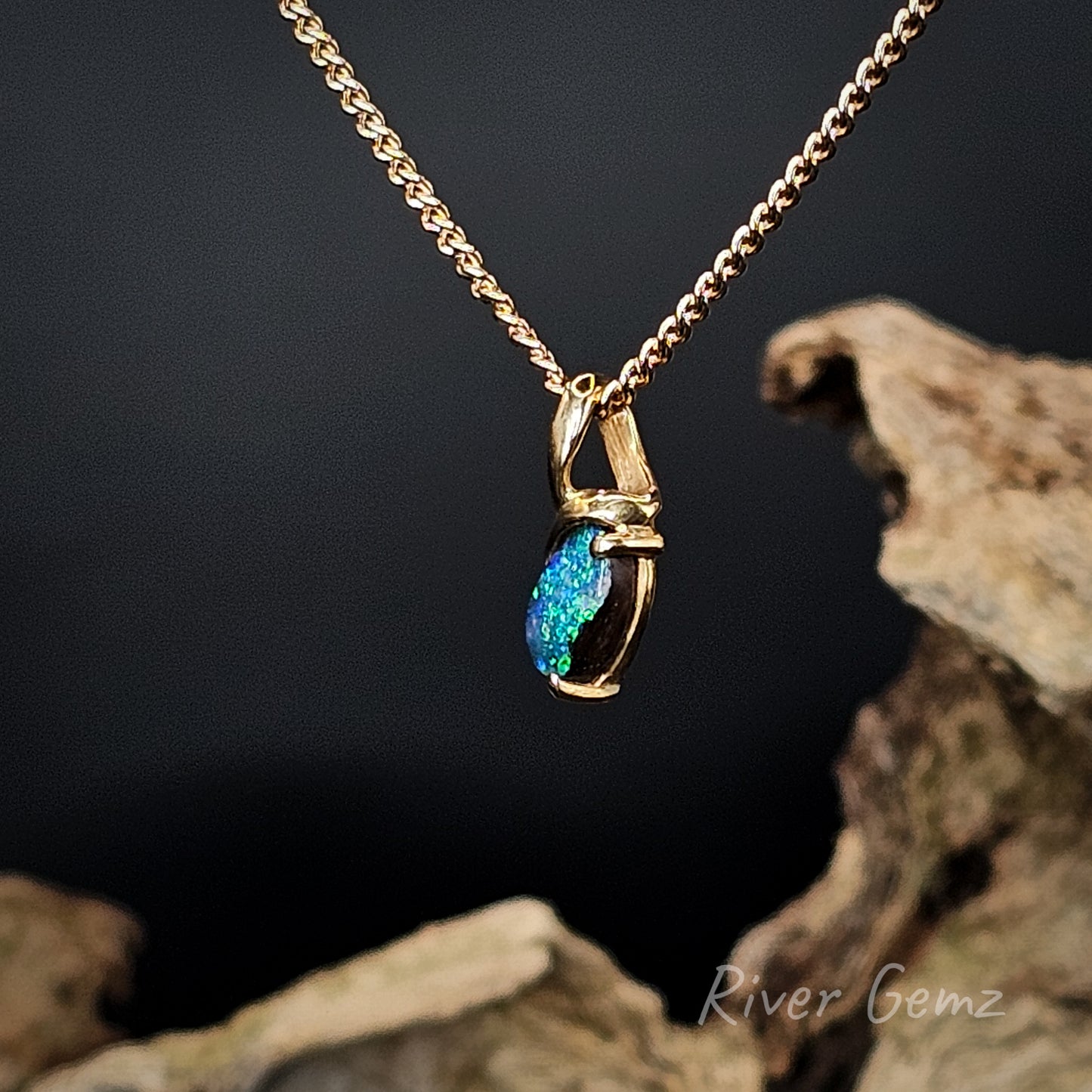 Side view shows the large eyelet of the hidden bail and the thickness of the boulder opal on a dark background