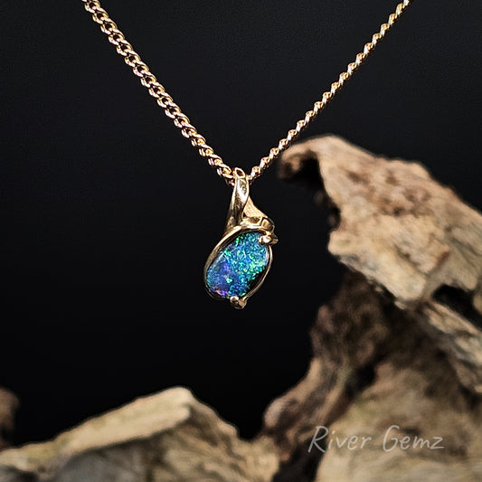 Gold necklace with a blue and green boulder opal on a dark background