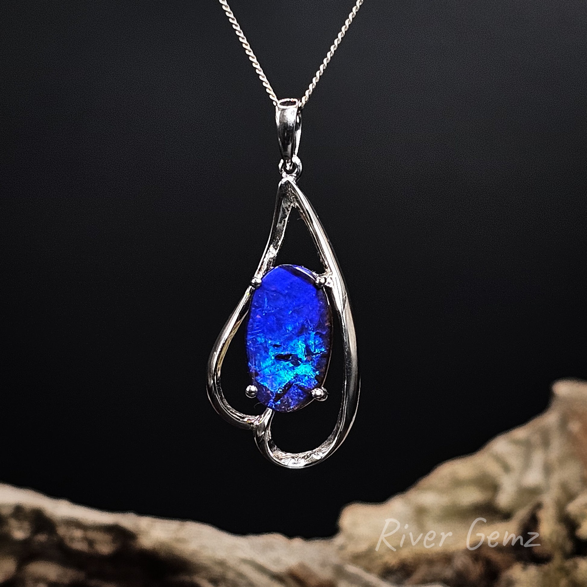 White gold pendant with a blue boulder opal on a dark background