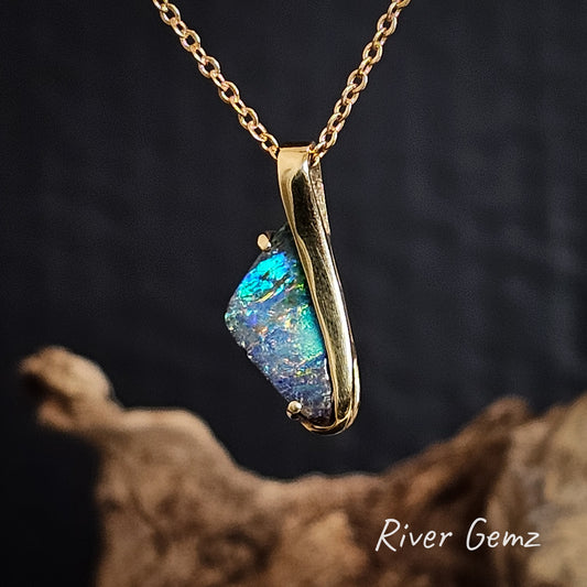 Gold necklace with a pendant featuring a colourful boulder opal on a dark background branded 'River Gemz'.