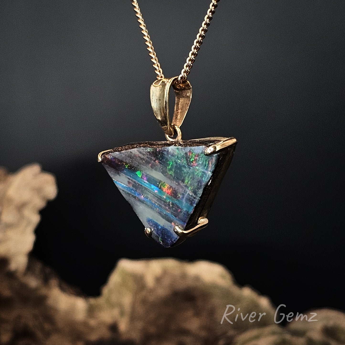 Triangle-shaped opal pendant on a gold chain against a dark background with 'River Gemz' branding.