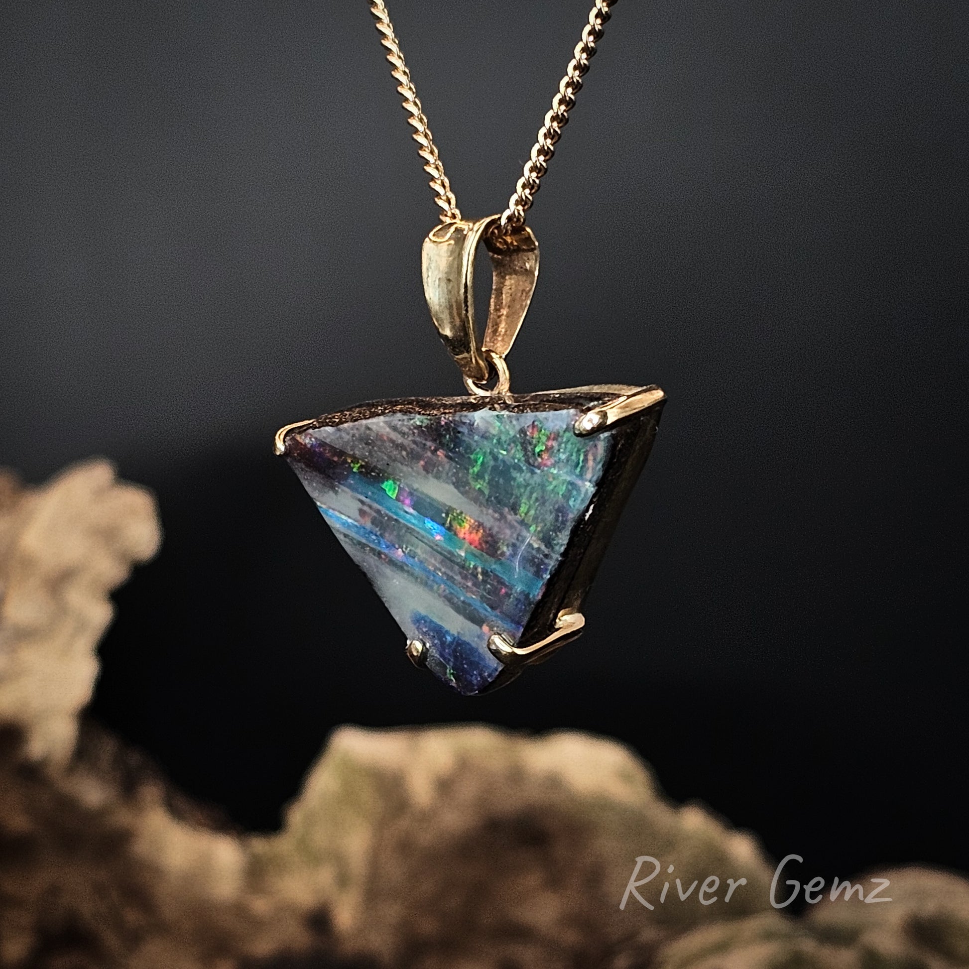 Triangle-shaped opal pendant on a gold chain against a dark background with 'River Gemz' branding.
