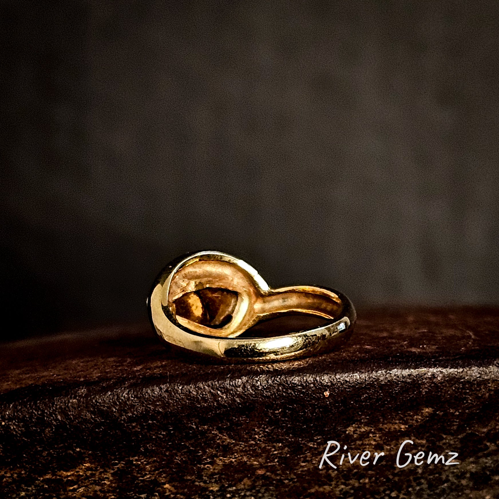 Gold ring showing the ironstone matrix at the back of the boulder opal on a dark surface with 'River Gemz' branding.