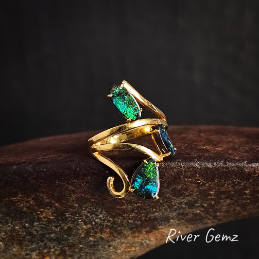 Gold ring with three blue and green boulder opals on a dark background, featuring the brand 'River Gemz'.