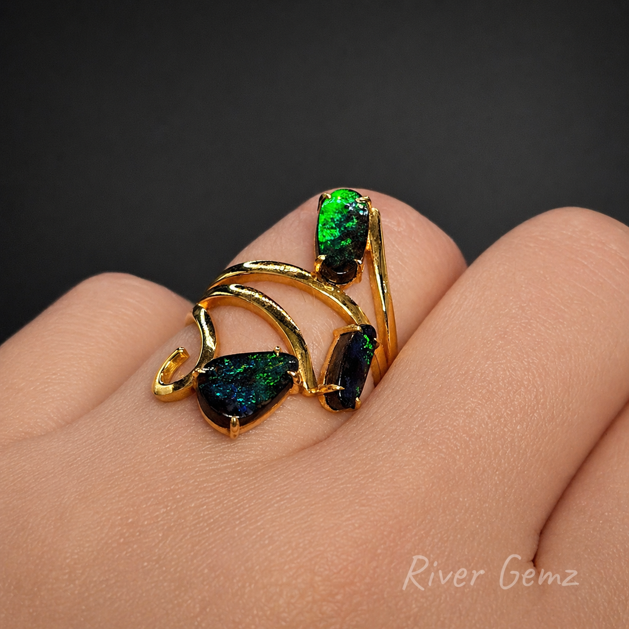 Ring with 3 opal stones set in yellow gold shown worn on ring finger.