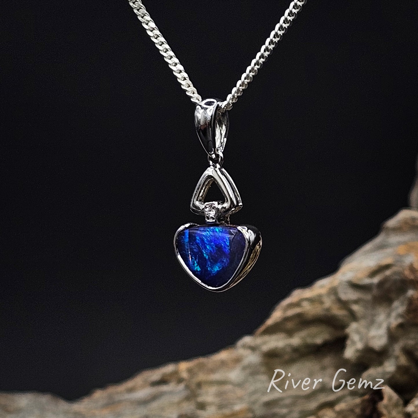White gold pendant with blue stone on a dark background with 'River Gemz' branding.