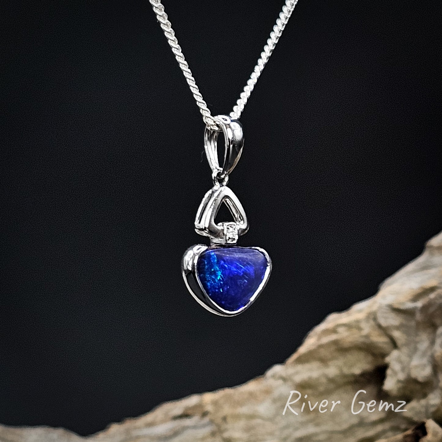 White gold pendant with a blue triangular-shaped boulder opal and diamond on a dark background