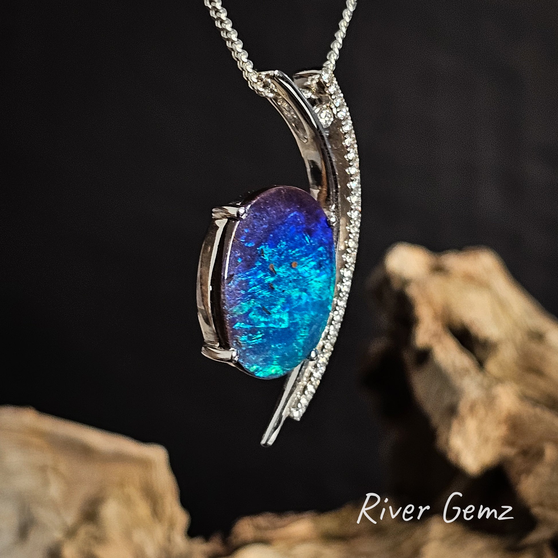 White gold pendant with a blue opal stone and channel set diamonds on a dark background, featuring 'River Gemz' branding.