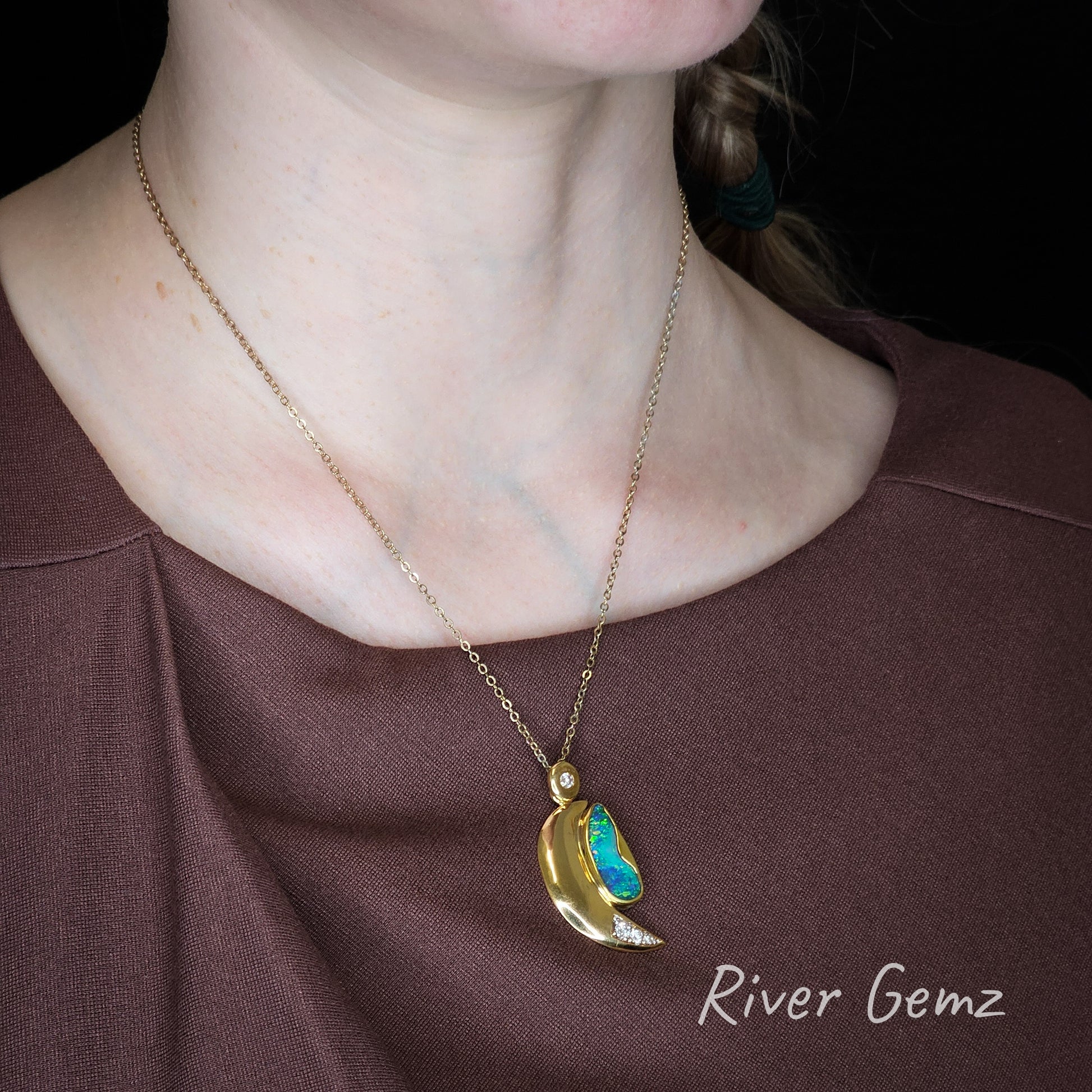 Necklace with an opal and diamond set in a crescent moon gold pendant worn by a person, brand 'River Gemz' visible.