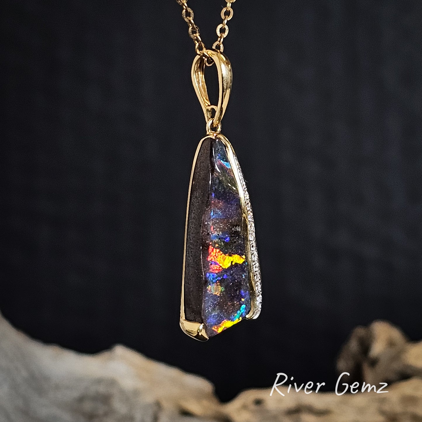 Slightly side on view of the opal pendant necklace with gold setting on a dark background, featuring the brand 'River Gemz'.