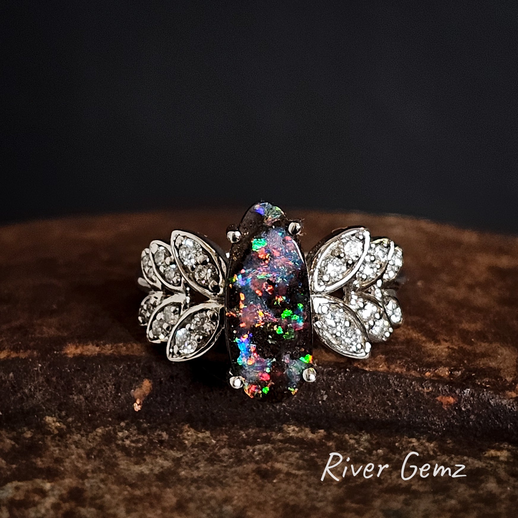 Boulder opal ring with diamond leaf designs on a dark background, branded 'River Gemz'.