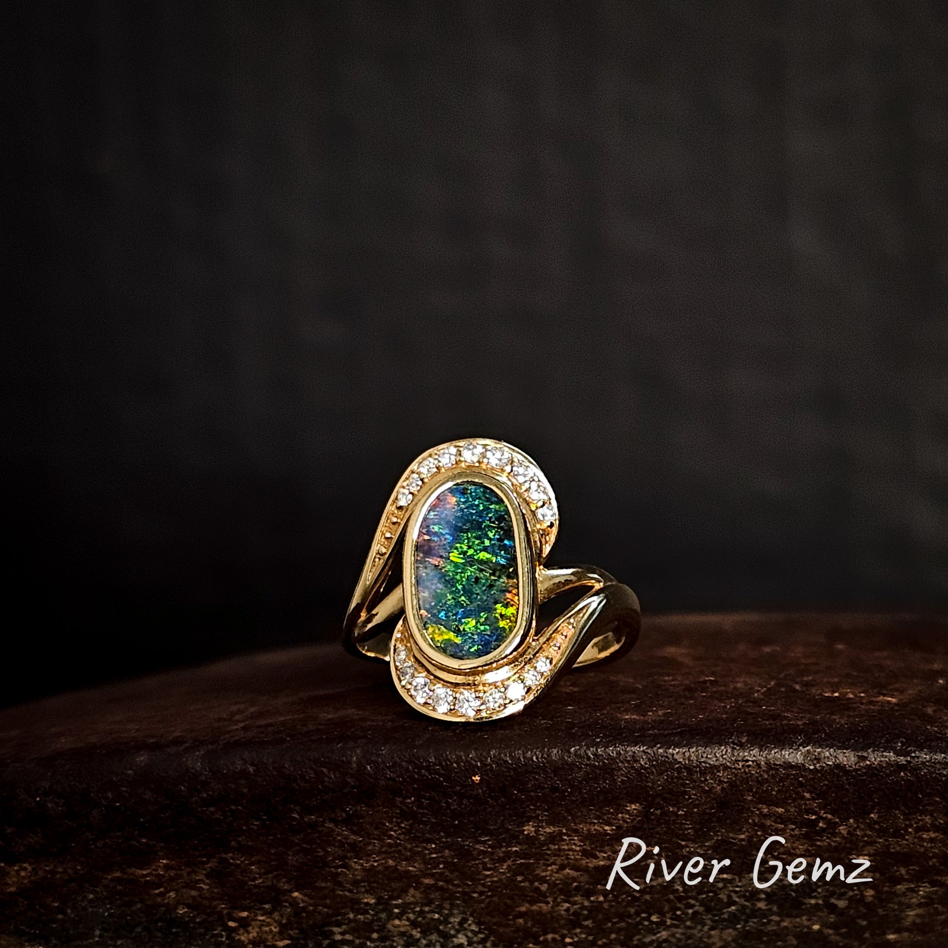 Gold ring with a multi-coloured boulder opal and diamonds on a dark background, featuring the brand 'River Gemz'.