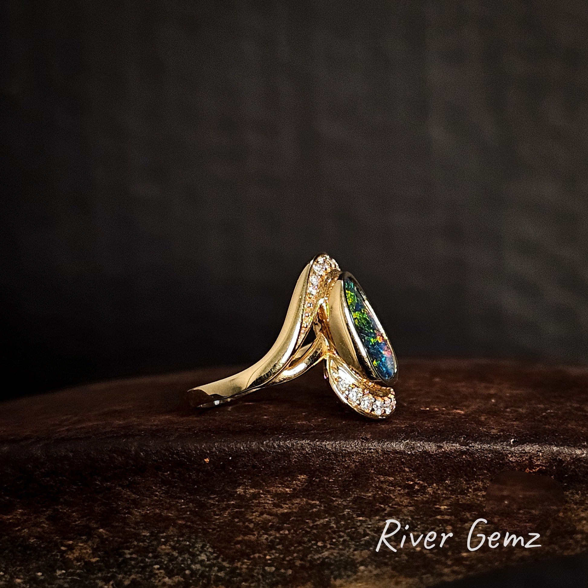 Side view of gold ring with an opal stone and diamonds on a dark surface, branded 'River Gemz'.