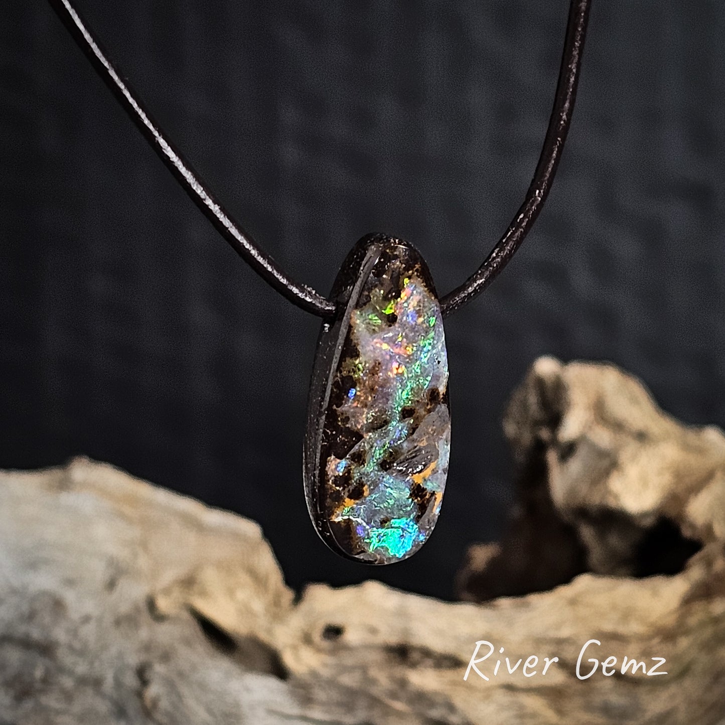 Side view of opal pendant showing the uniform thickness of the stone on a brown cord with a dark background and 'River Gemz' branding.