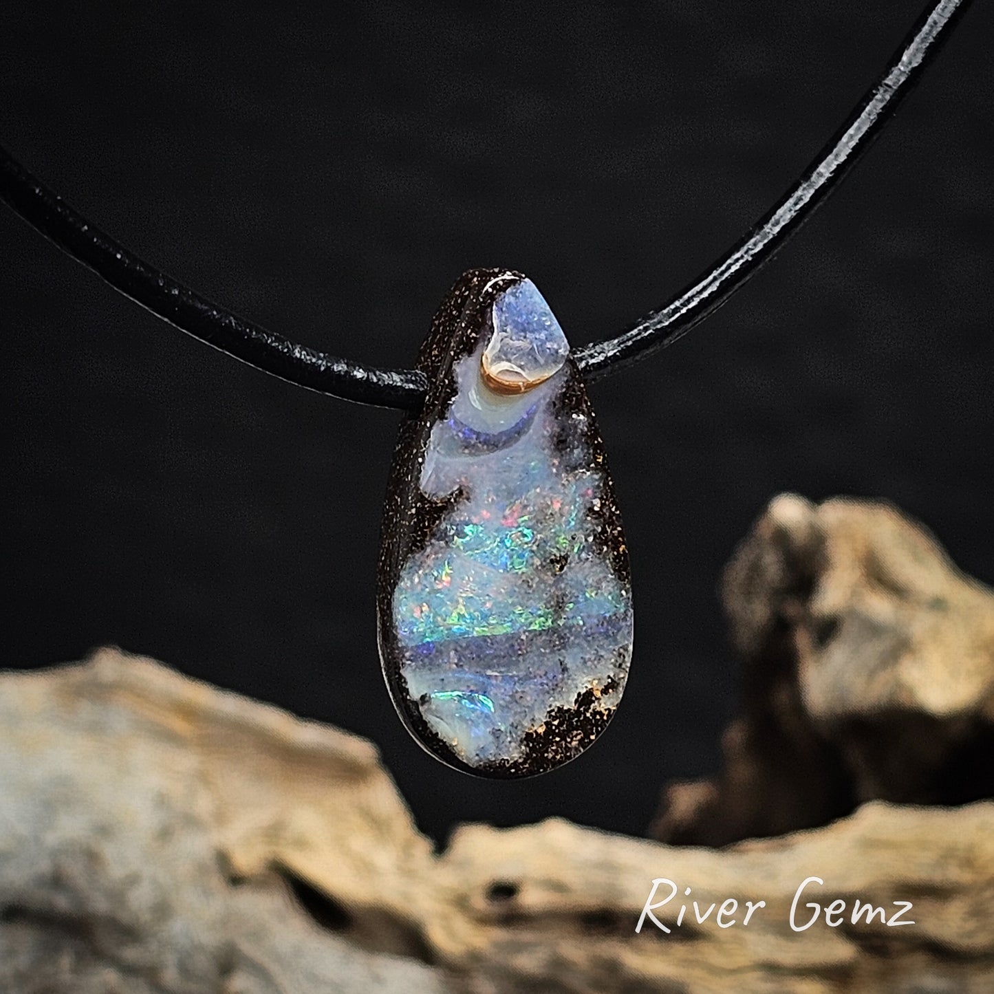 Tear-drop shaped opal pendant on a brown cord with a blurred natural background.