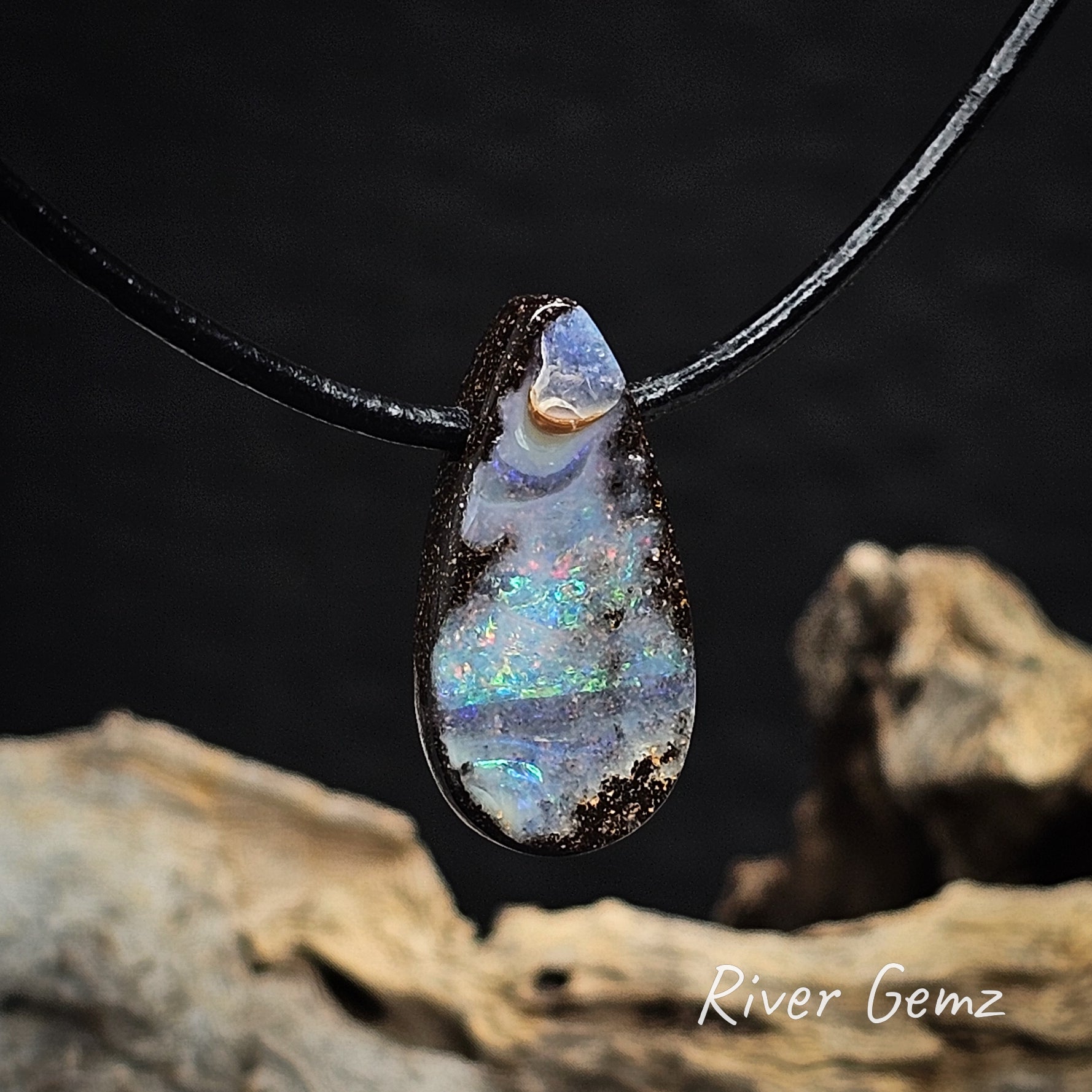 Tear-drop shaped opal pendant on a brown cord with a blurred natural background.