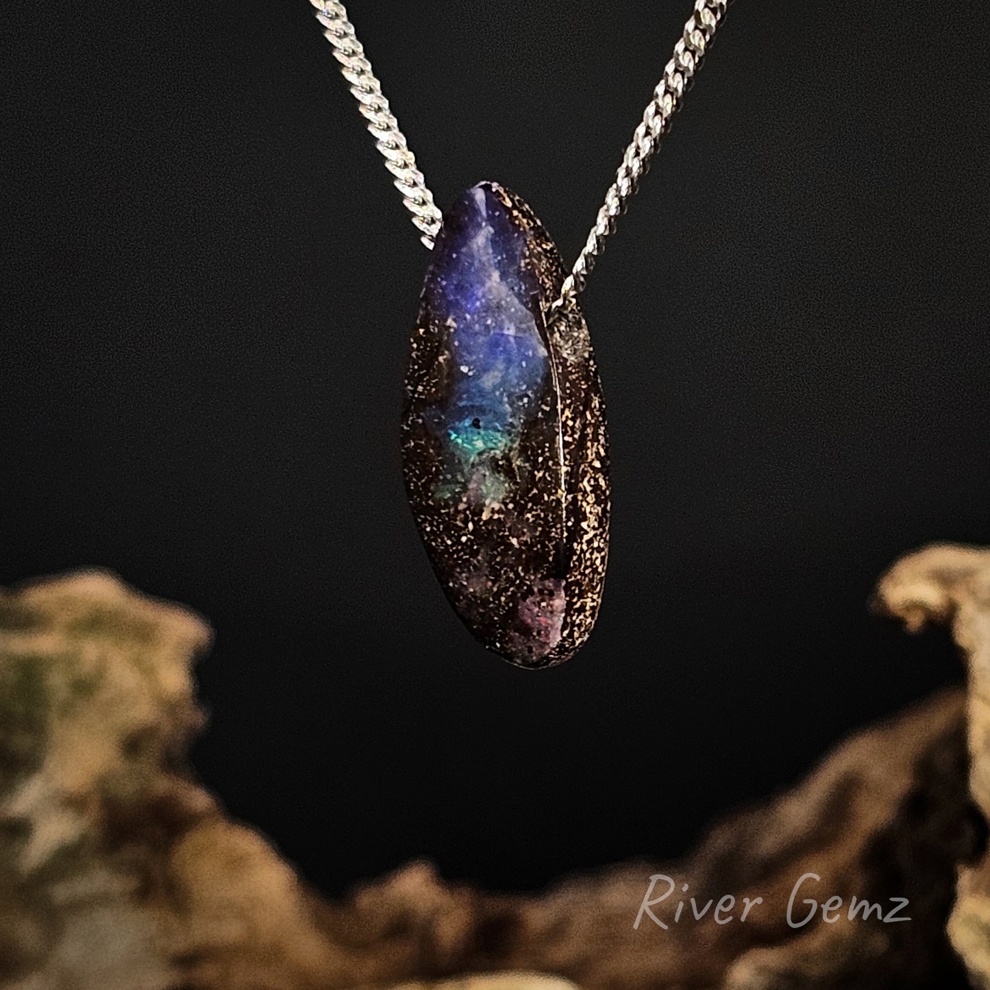 Necklace with a colorful pendant on a dark background, featuring the brand 'River Gemz'.