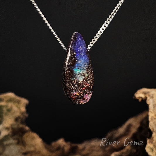 Teardrop-shaped pendant with multicolor gemstone on a chain against a dark background