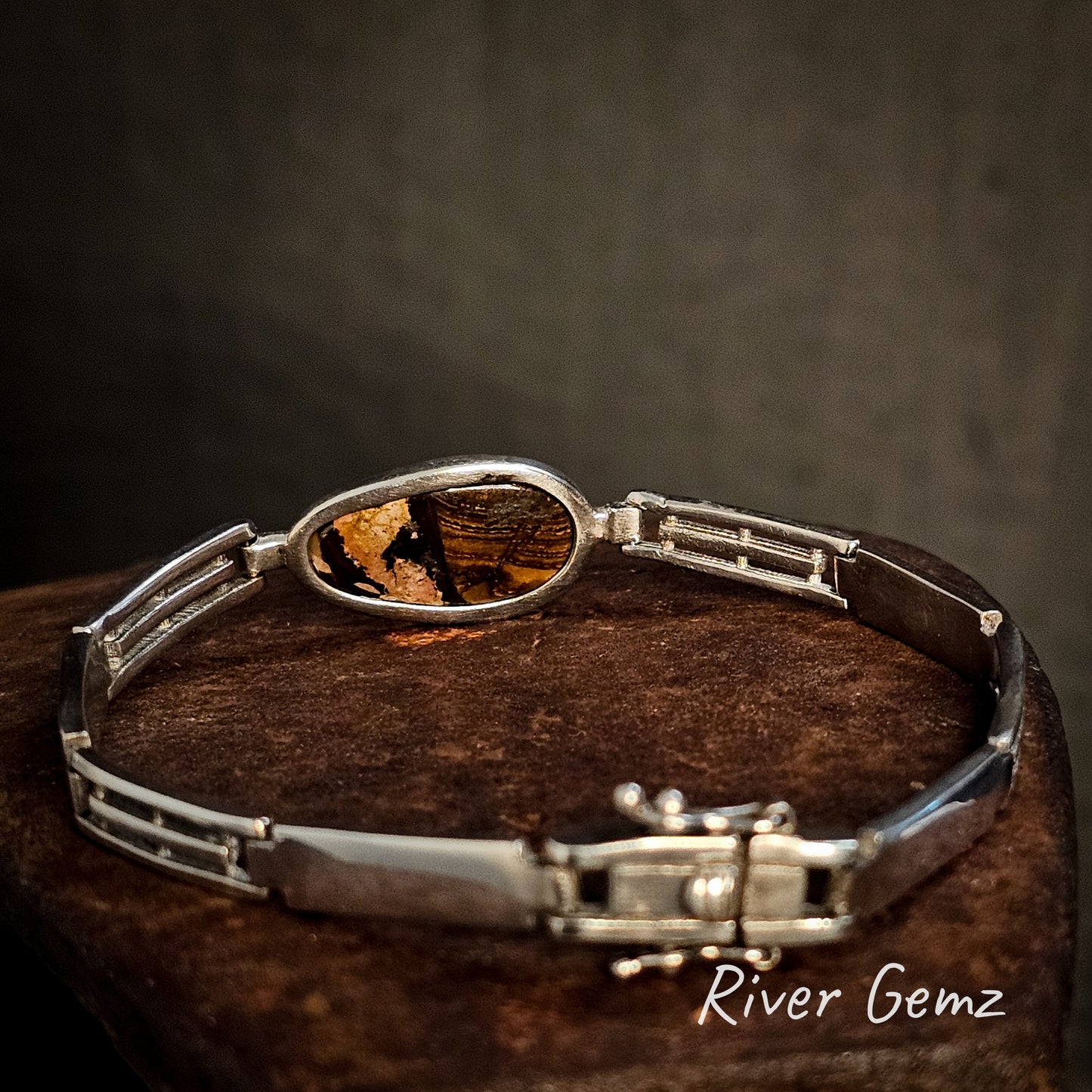 Silver bracelet with the back of the boulder opal showing the ironstone matrix on a dark surface, branded 'River Gemz'.