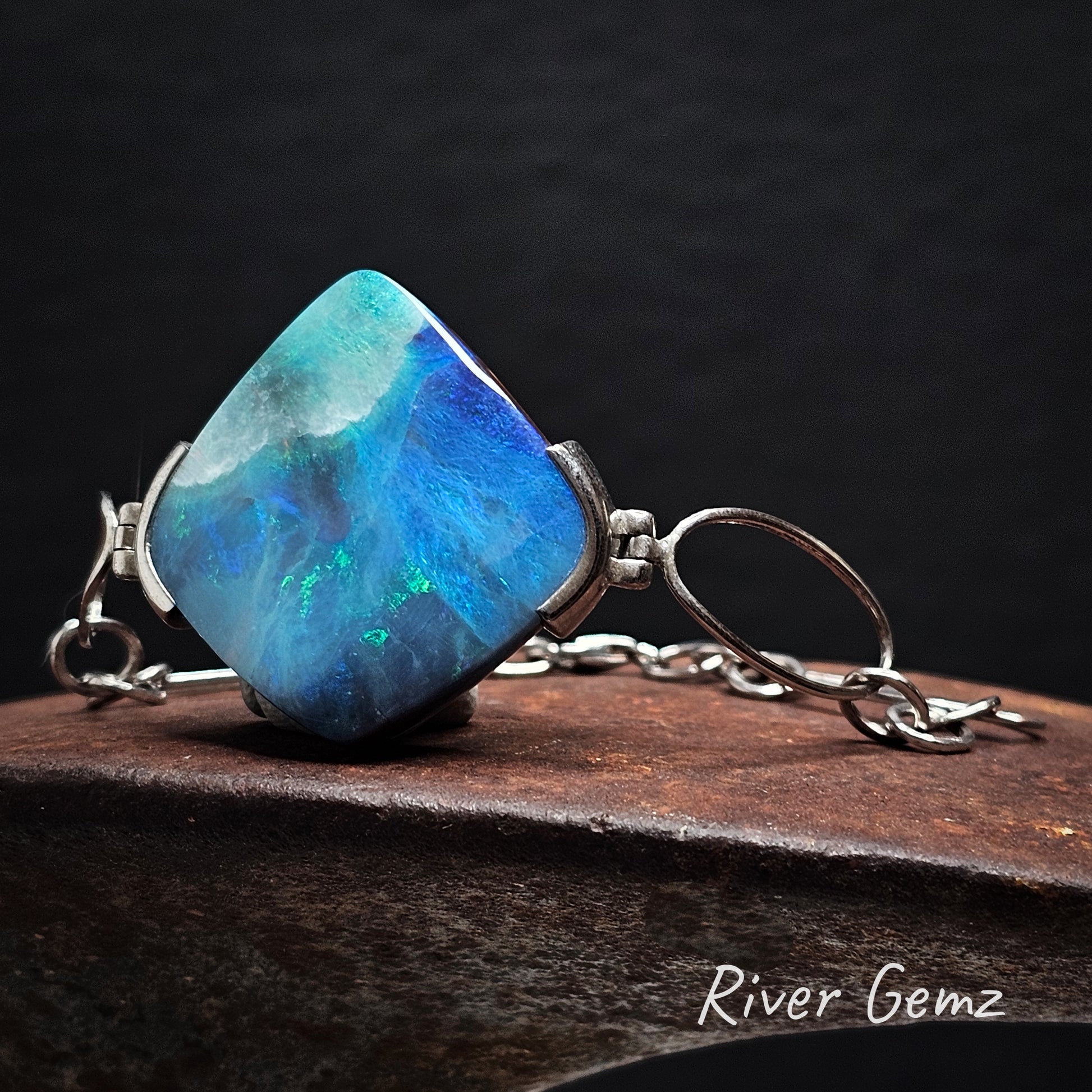 Silver bracelet with a large blue and green stone on a dark background, featuring the brand 'River Gemz'.