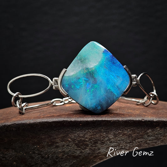Blue boulder opal partial besel set in sterling silver bracelet on a dark background with 'River Gemz' branding.