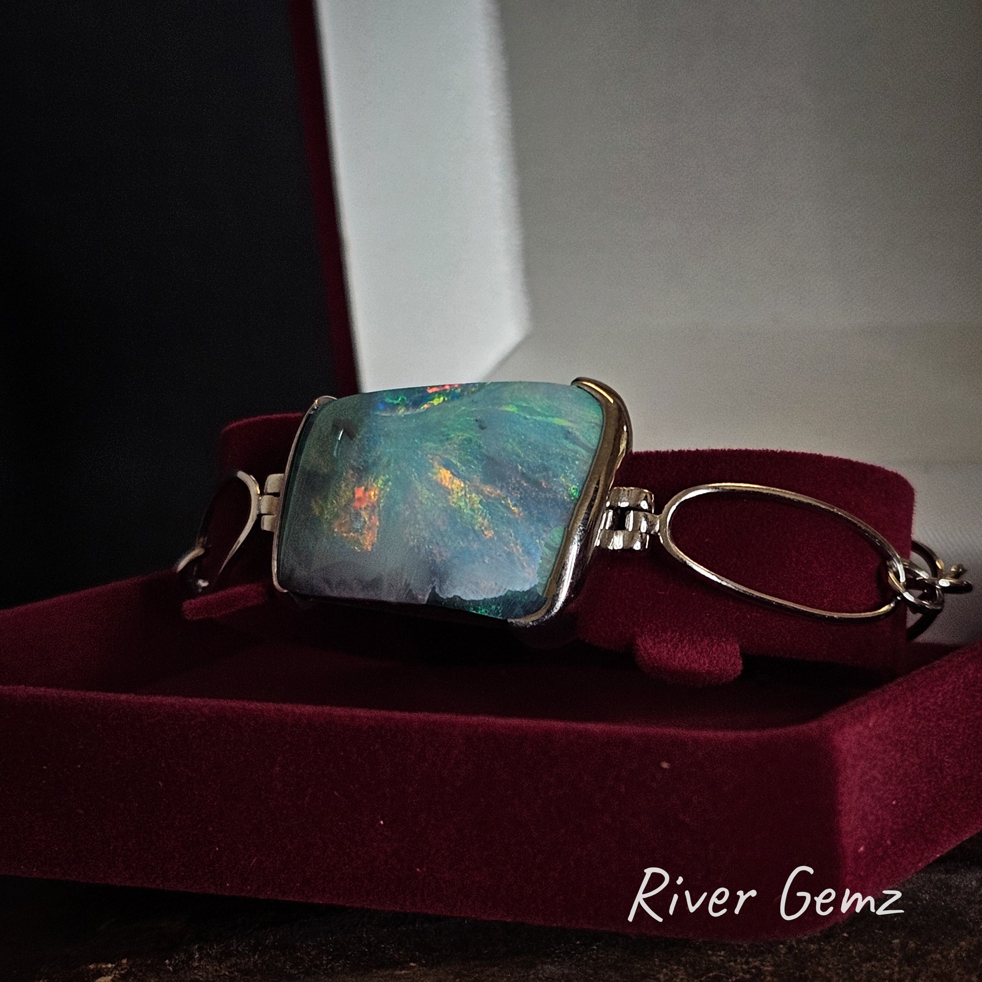 Bangle with a colourful gemstone on a red cushion, branded 'River Gemz'.