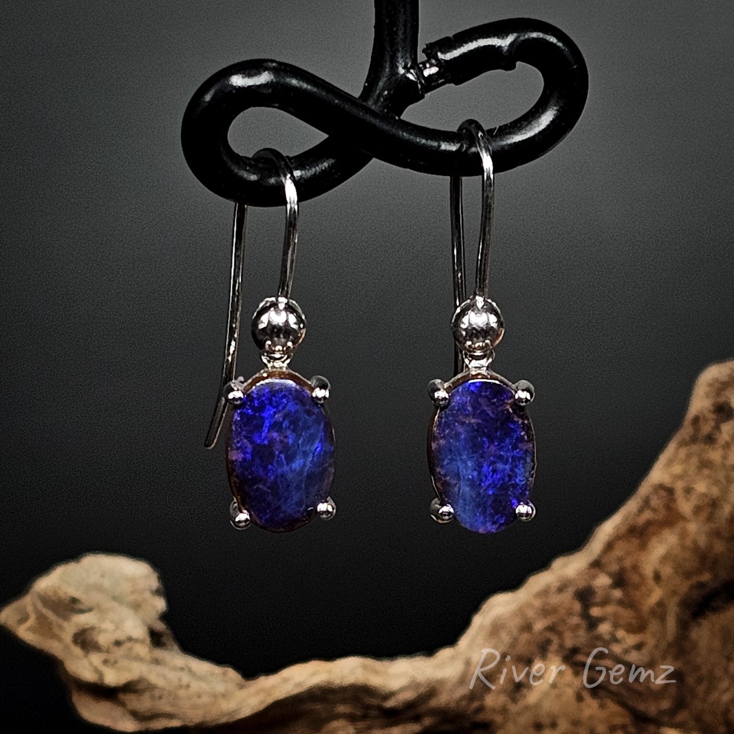 Oval shaped dark blue opals claw set in silver dangly earrings.