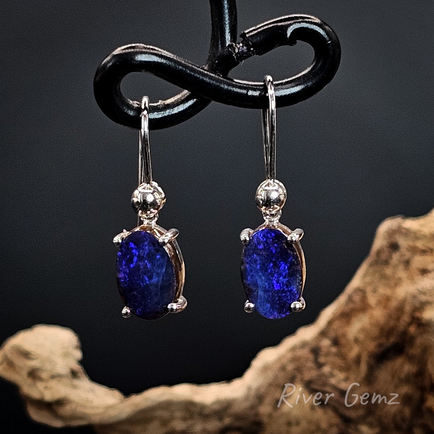 Purple coloured opals set in silver shepherd hooks against a dark background.