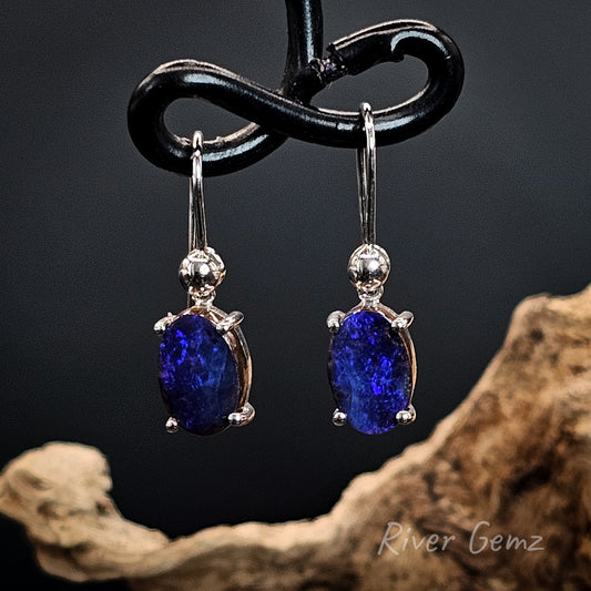 Purple coloured opals set in silver shepherd hooks against a dark background.