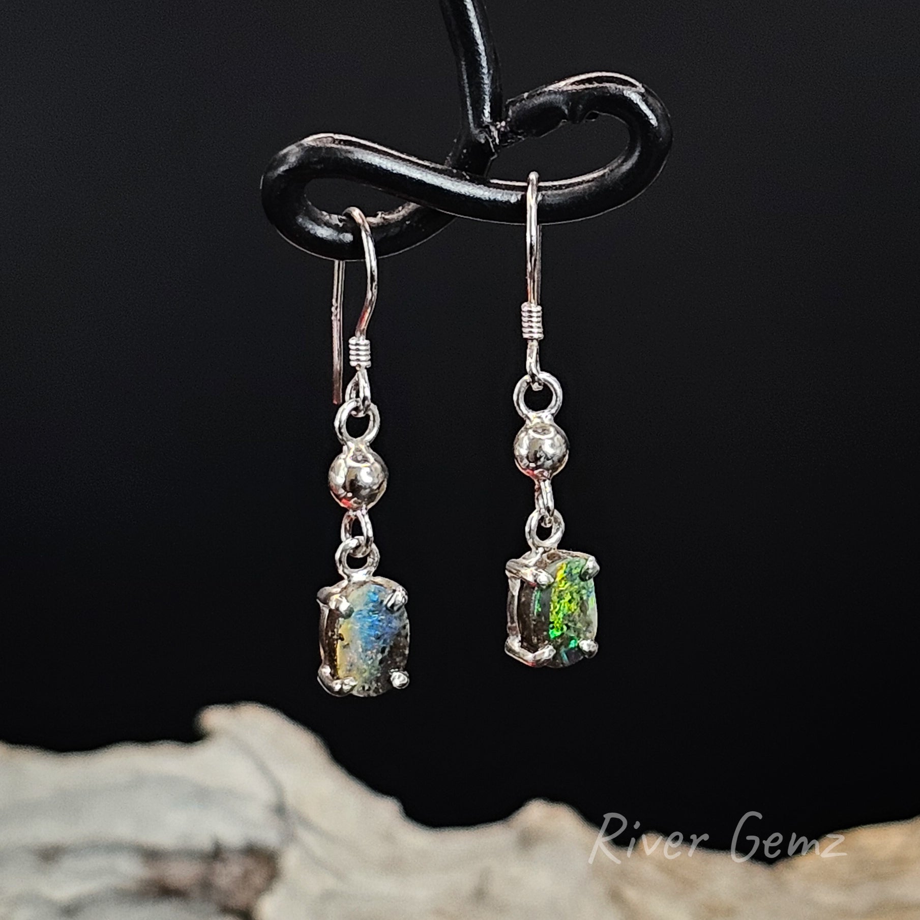 Silver earrings with multi-coloured boulder opals on a black background