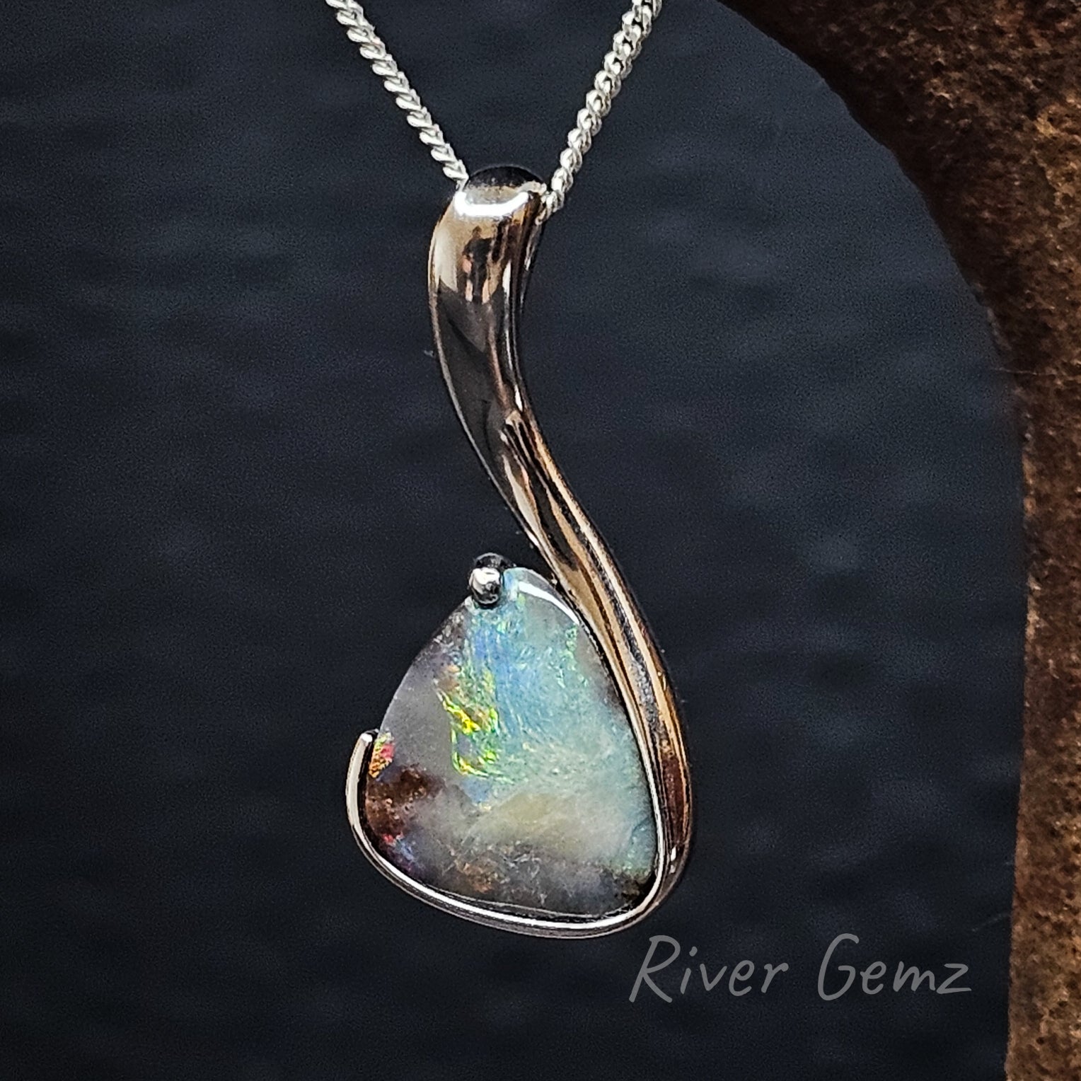 Large triangular shaped boulder opal in a hook shaped silver pendant.