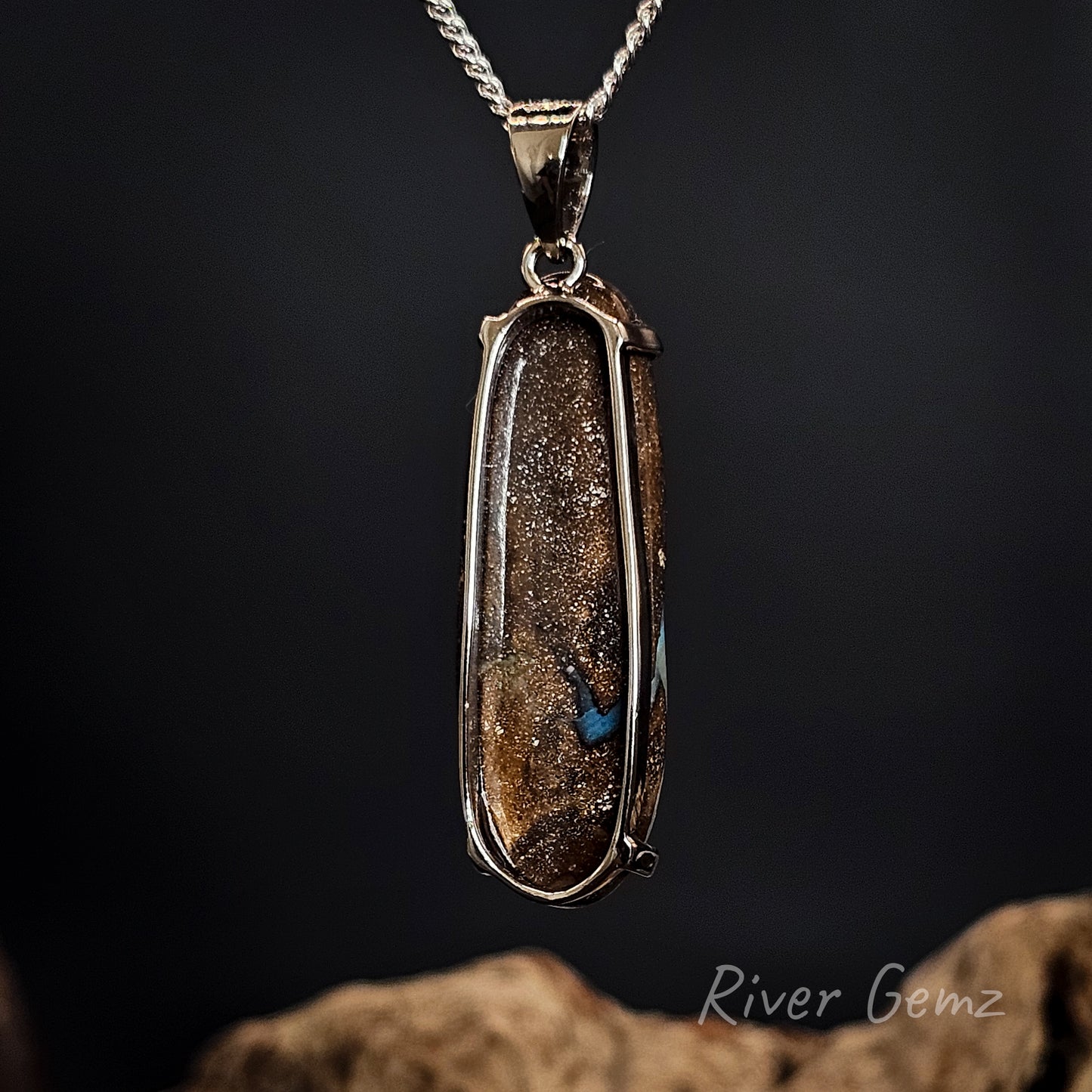 Rear view of silver pendant showing the ironstone matrix of the boulder opal set in it on a dark background