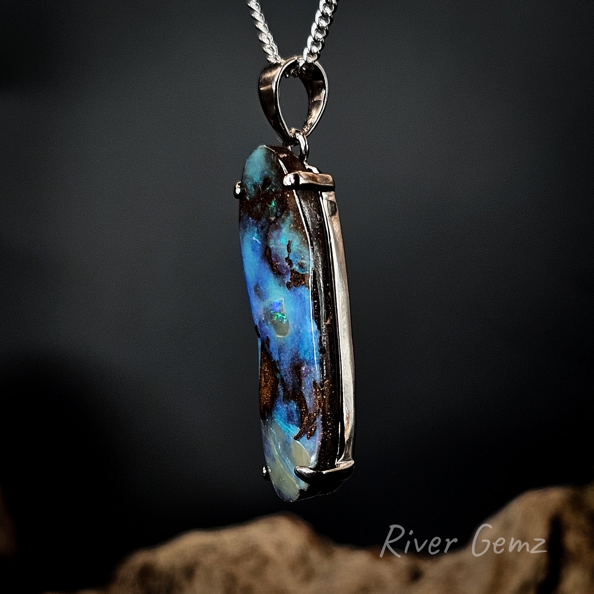 Boulder opal necklace set in sterling silver on a chain with a dark background