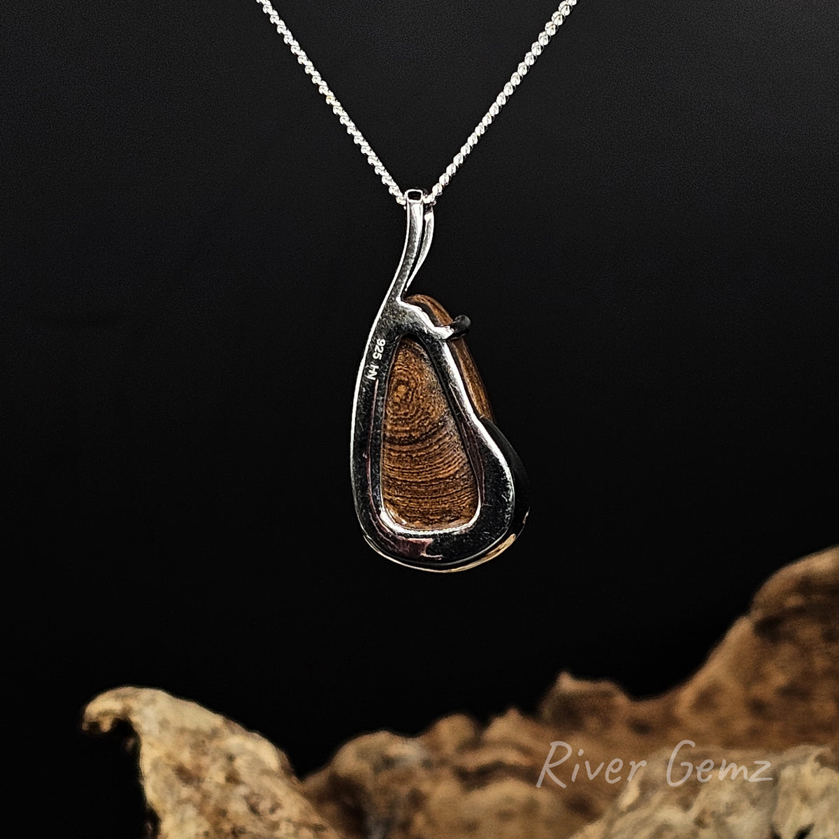 Rear view of the necklace showing the brown ironstone matrix of the boulder opal, suspended from a silver chain against a dark background with a piece of driftwood at the bottom.