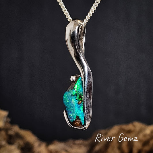 Silver necklace with a blue gemstone on a dark background, branded 'River Gemz'.