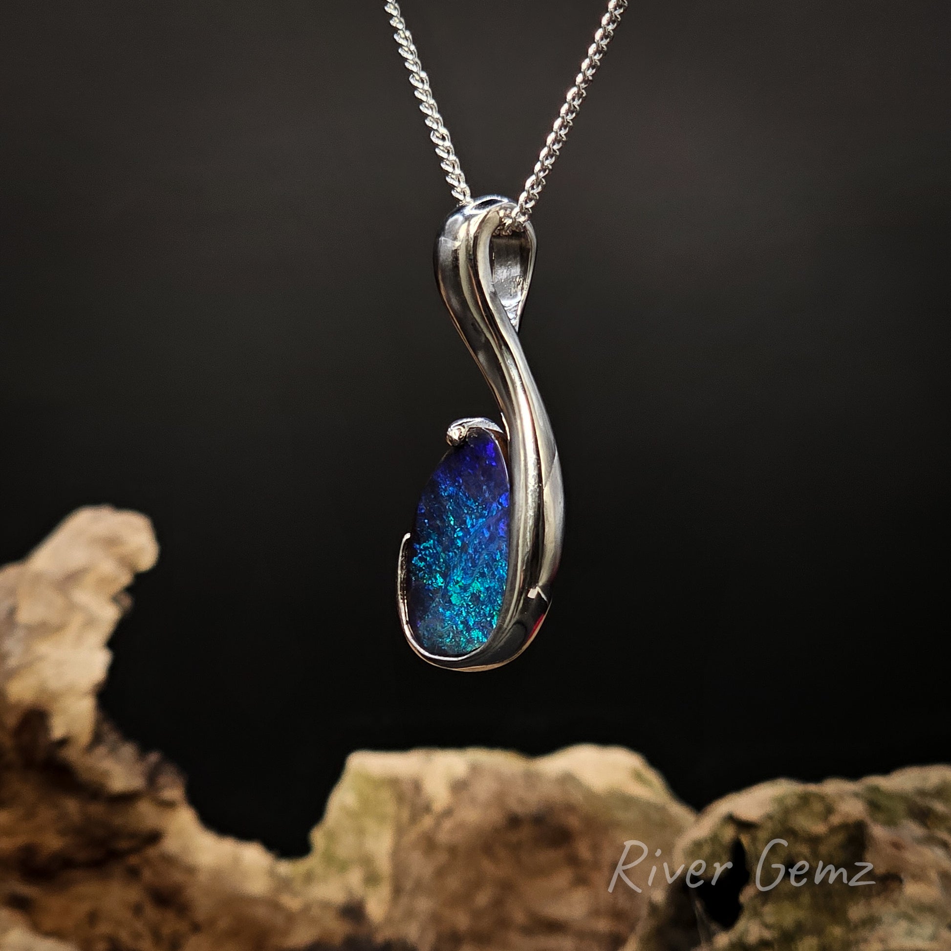 Silver pendant with blue boulder opal on a dark background