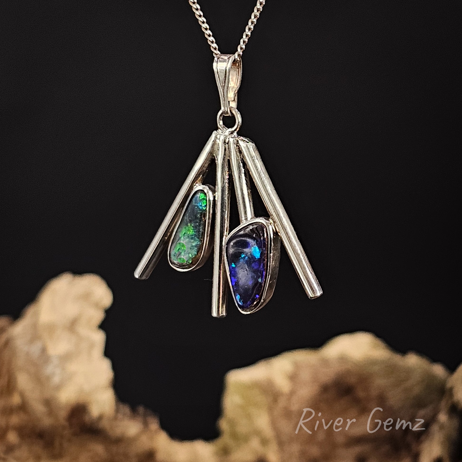 Silver pendant with embedded blue and green boulder opals on a dark background