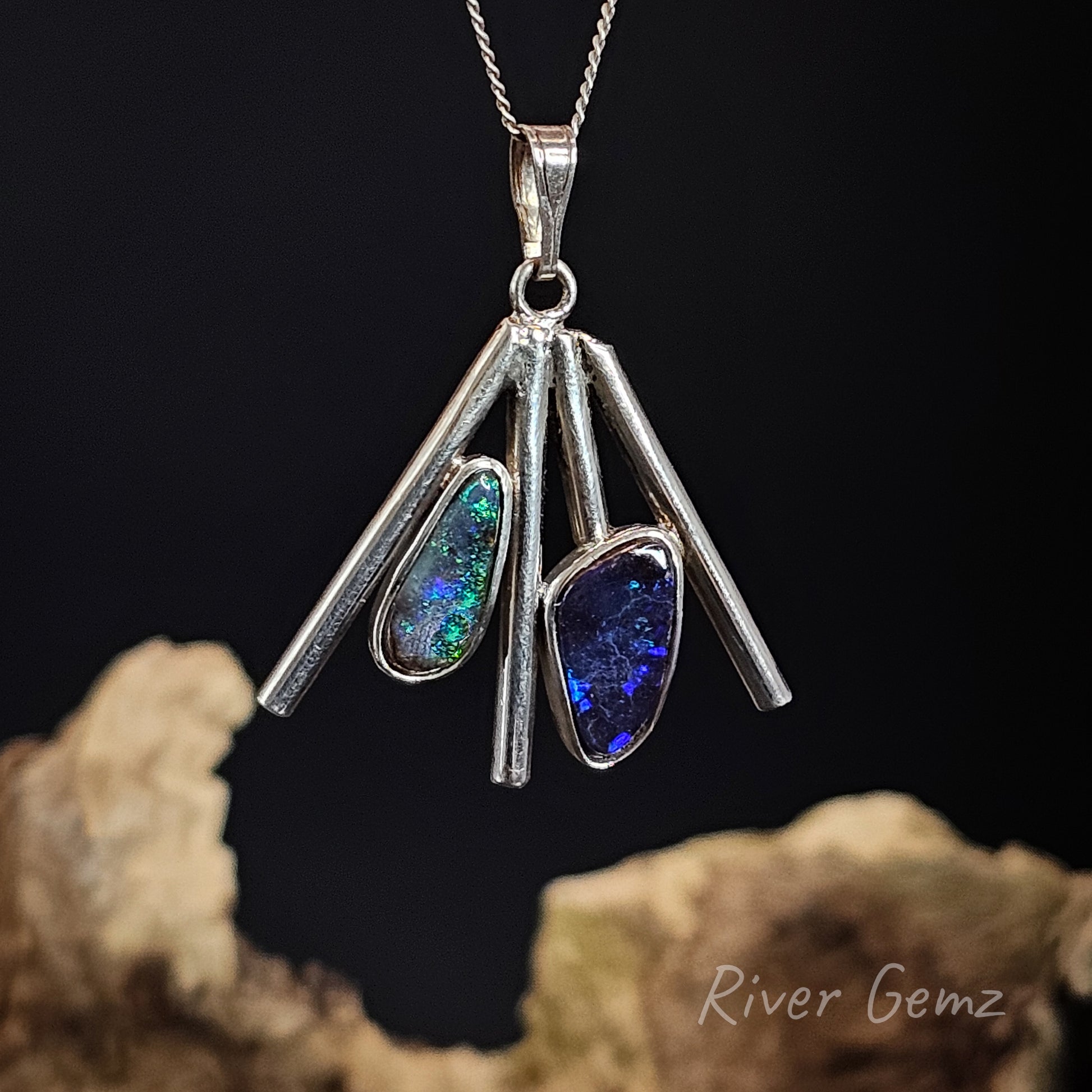 Silver pendant with colorful stones on a dark background, featuring 'River Gemz' branding.