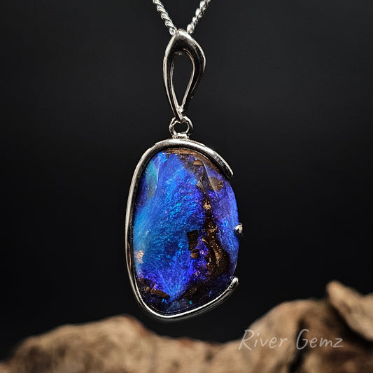 Blue boulder opal pendant with silver setting on a dark background