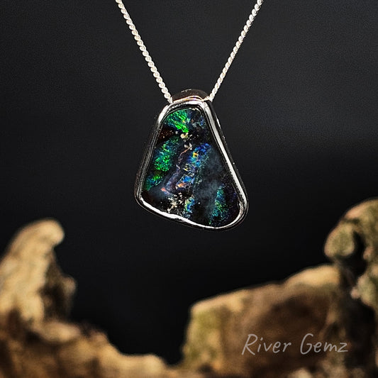 Free-form cut boulder opal set in sterling silver pendant on a dark background with 'River Gemz' branding.