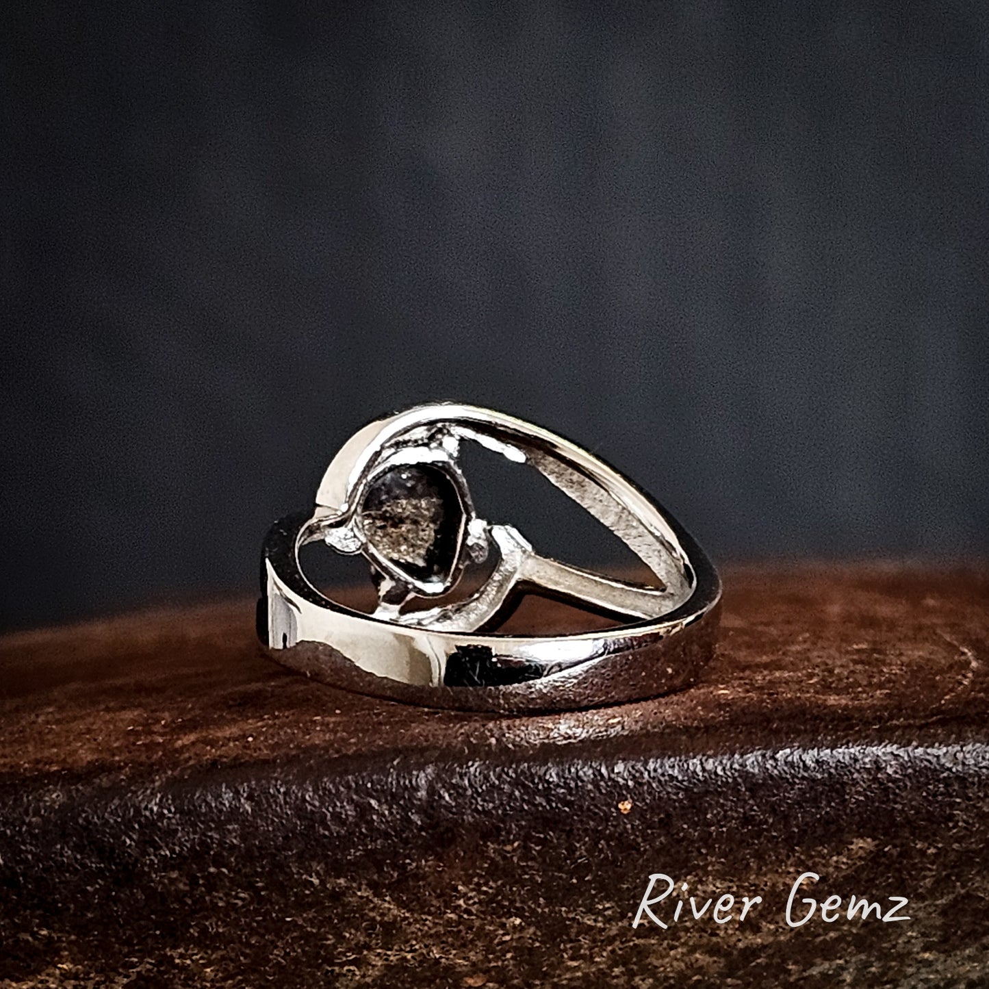 Rear view of silver ring showing the ironstone matrix of the boulder opal on a dark surface, branded 'River Gemz'.
