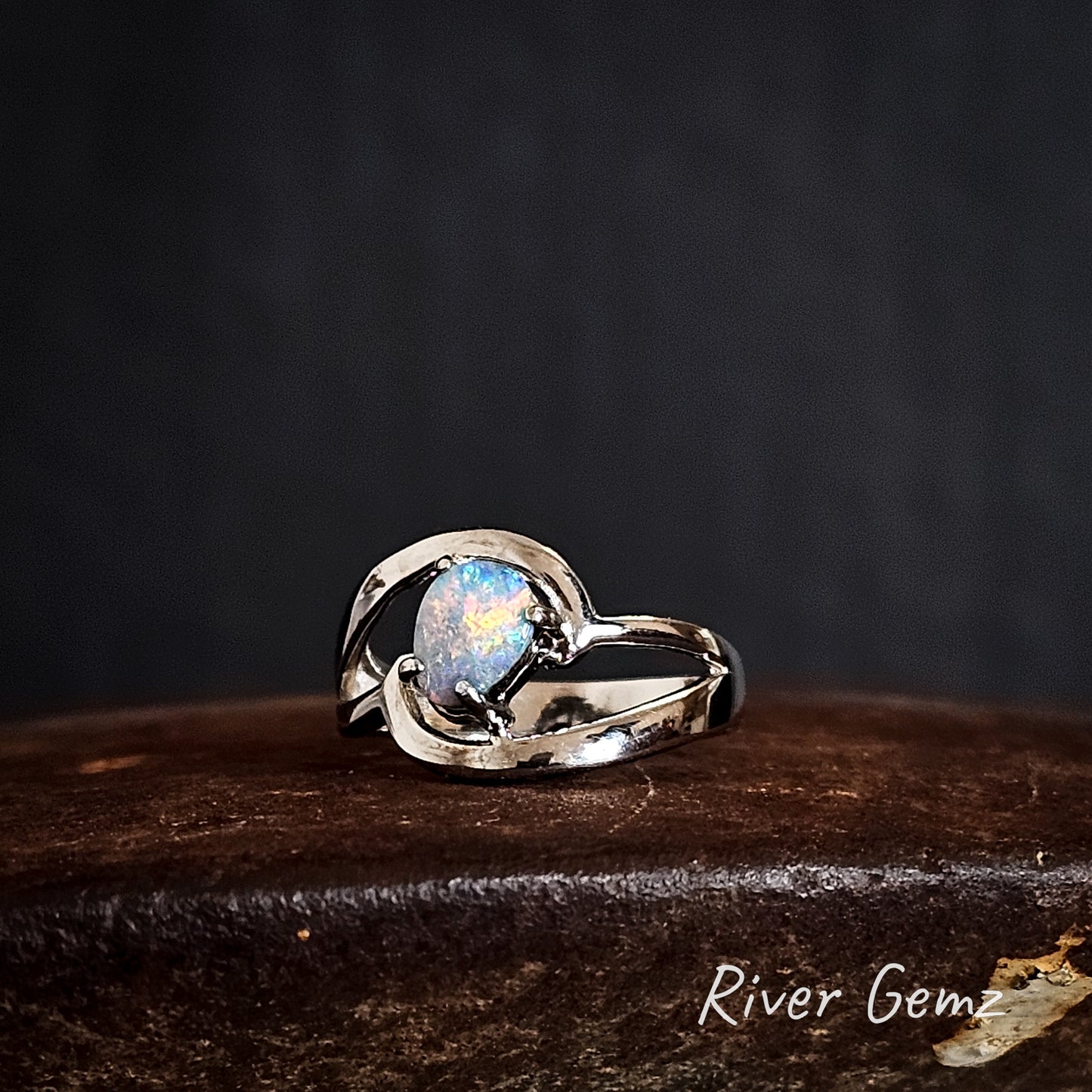 Silver ring with a colourful boulder opal on a dark background, branded 'River Gemz'.